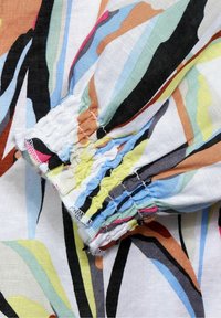 Tissu en coton présentant des motifs abstraits multicolores, avec des poignets froncés en jaune pastel, bleu, rose, et des accents noirs.