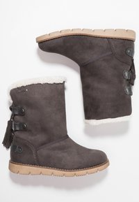 Bottines en daim gris avec une doublure en fausse fourrure, un pompon sur le côté et des accents de boutons. Semelle en caoutchouc avec un design texturé antidérapant.