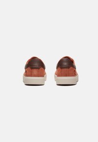 Calzature con tomaia in suede di colore ruggine, accentata da un inconfondibile tacco in pelle marrone e una suola in gomma bianca con cuciture tonali.