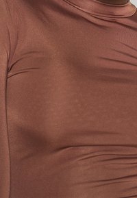 Pitkähihainen paita rikkaan ruskeassa sävyssä, jossa on sileä, kiiltävä pinta ja vartalonmyötäinen malli, joka korostaa kankaan muotoja.