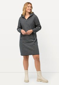Vestido con capucha a rayas en navy y crema, de mangas largas, con bolsillos frontales y un corte holgado, combinado con botas de tobillo beige.