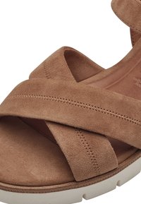 Brown suede sandal featuring cross straps, a cushioned footbed, a light-colored textured sole, and visible stitching details.