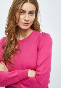 Maglione rosa aderente con maniche lunghe, polsini a costine e scollatura rotonda. Texture morbida con un delicato dettaglio a sbuffo sulle cuciture delle spalle.