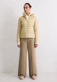 Lichtbeige donzen jas met een hoge kraag, ritssluiting en horizontale stiknaden, gecombineerd met beige broek met wijde pijpen en crèmekleurige sneakers.