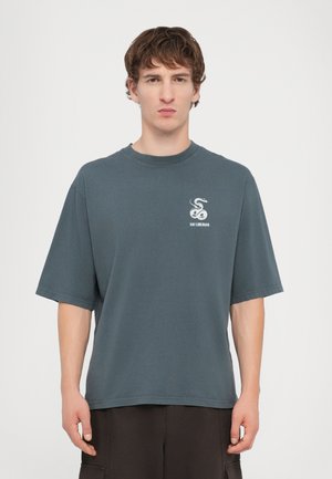 Dark teal oversized t-shirt made of cotton, featuring a round neck and short sleeves. A small white snake graphic is printed on the chest.