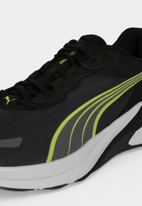Μαύρο και γκρι αθλητικό παπούτσι Puma με νέον κίτρινη ρίγα, μαύρα κορδόνια και λευκή σόλα, εμφανιζόμενο από πλάγια και πάνω γωνία.