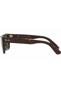 Occhiali da sole tartaruga con una montatura spessa, lenti scure e il marchio Ray-Ban sulle astine. Fabbricati in Italia con una finitura lucida.