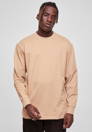 Hosszú ujjú bézs t-shirt, pamut keverékből készült; kerek nyakkivágással, laza fazonnal és minimális varrási részletekkel a ujjakon.