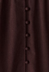 Dyb rødbrunt tekstil med en lodret række stofbetrukne knapper, med et tekstureret linnedudseende og glat stikningsdetalje.