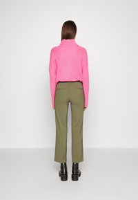 Maglione fucsia a maglia con colletto alto abbinato a pantaloni sartoriali verde oliva e stivali platform neri lucidi. Texture morbide, vestibilità rilassata.