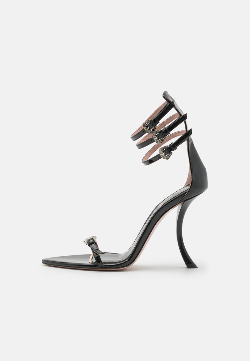 Sándalo de charol negro de tacón alto con punta cuadrada, tres correas ajustables en el tobillo y un tacón stiletto contorneado.