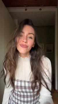 Maglia crema a maniche lunghe con motivo a rilievo, indossata sopra un vestito a quadri in tonalità di bordeaux e bianco, abbinata a capelli mossi e sciolti.