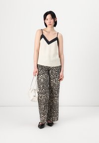 Camiseta de crema clara con un acento negro en forma de V, combinada con pantalones anchos a rayas de cebra en blanco y negro. Bolso blanco y zapatos negros.