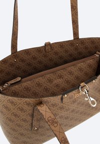 Bolso de mano marrón con estampado y detalles en cuero sintético. Incluye un bolsillo interior con cremallera y acentos de metal. Impresión del logo visible en la parte frontal.