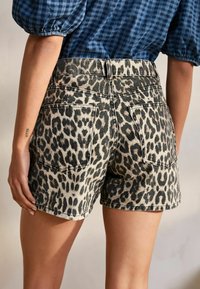 Shorts en denim imprimé léopard avec une taille mi-haute, comportant des poches arrière et un ourlet effiloché. Le tissu a une texture lisse et un motif audacieux.