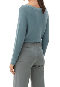 Suéter azul acanalado con un escote amplio, combinado con pantalones grises que cuentan con dos bolsillos traseros. La tela parece suave con un acabado texturizado.