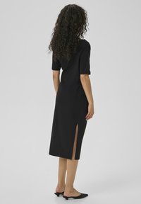 Black midi dress with short sleeves, featuring side slits and a form-fitting design. Smooth texture and simple, minimalist style.