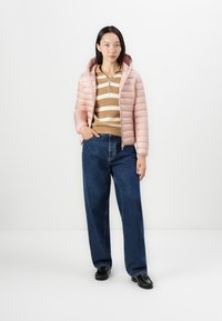 Lys rosa pufferjakke med hette, med glidelås foran, brukt over en beige og hvit stripete genser, kombinert med blå høytlivsjeans. Sorte sko.