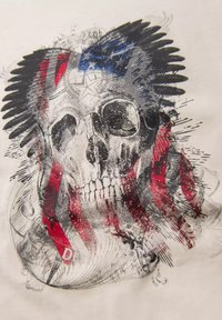 Grafisk T-shirt med et kraniumdesign, der integrerer røde og blå elementer med et flagmotiv, sat mod en cremet baggrund med teksturerede detaljer.
