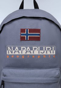 Pilkai audiniai kuprinė su išsiuvinėtu Norvegijos vėliavos pleistru ir balta "NAPAPIURI geographic" logotipu su oranžinėmis detalėmis.