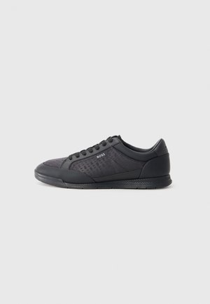 Black sneakers with a textured fabric upper, smooth leather accents, round toe, and rubber sole featuring a patterned tread design.