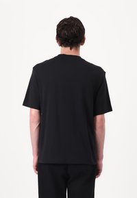 Sort kortærmet t-shirt, afslappet pasform, blødt bomuldsstof, rund hals, glat tekstur, ingen mønstre eller synlig branding. Bageste udsigt vist.