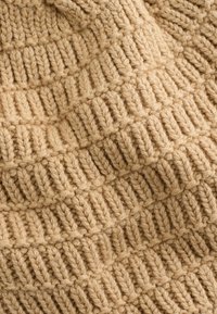 Fed chunky beige garn med et ribbet, tekstureret mønster, der har lodrette og diagonale rækker, som skaber en hævet, vævet effekt.