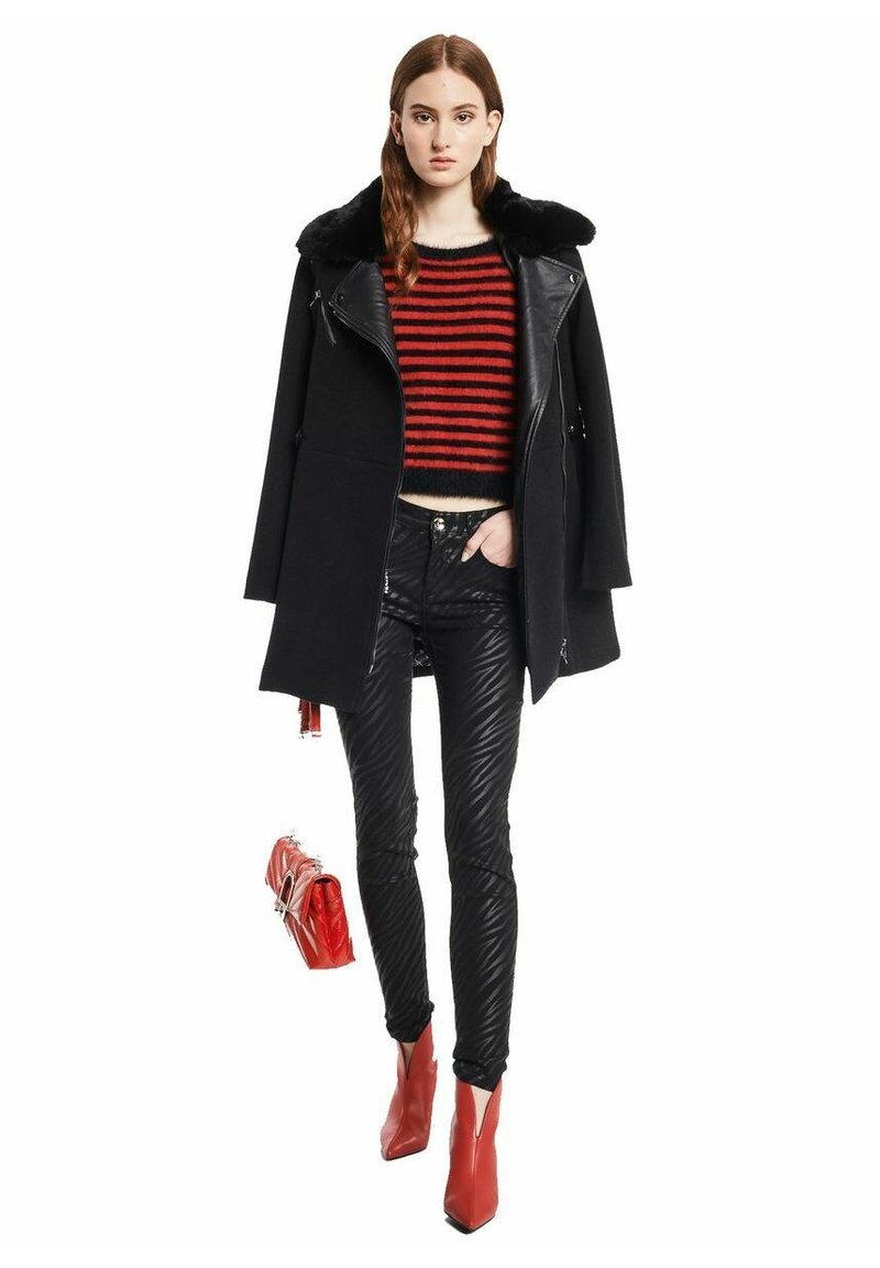 Zwarte wollen jas met nepbont kraag, rood en zwart gestreepte cropped sweater, geplooide zwarte leren broek, rode haklaarzen en handtas.