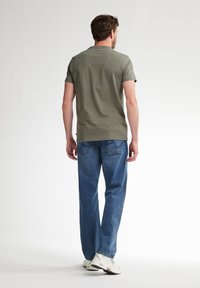 Olijfgroene t-shirt met korte mouwen voor heren, gemaakt van zacht materiaal, gecombineerd met losse blauwe jeans en witte sneakers. Casual pasvorm.