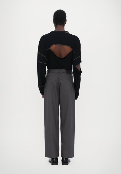 Black long-sleeve top with a large cutout and gray stitching, paired with gray wide-leg trousers and black shoes. Simple design, casual fit.