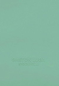 Cestovná taška v mäton zelenom odtieni s textúrovaným materiálom a embosovaným logom "GASTON LUGA STOCKHOLM" na spodnej strane pre identifikáciu značky.