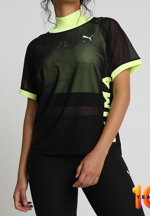Frau trägt ein schwarzes, transparentes PUMA-T-Shirt mit neon-gelbem Kragen und Ärmelsäumen, kombiniert mit schwarzen, gerippten Leggings.