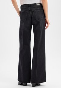 Szerokie, czarne jeansy z denimu o fakturowanym wykończeniu i naszywką z logo w pasie. Na plecach widoczne są cztery kieszenie.
