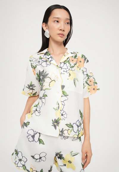 Blomst broderet kortærmet skjorte i hvid, udstyret med farverige blomster, gul kant og en knap-ope design. Sættet kombineres med matchende shorts.