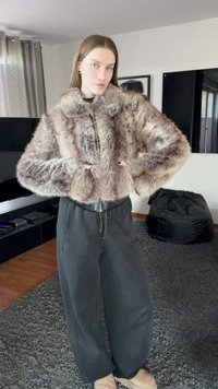 Giacca corta in pelliccia sintetica con motivo marrone e crema, dotata di chiusura con zip e orlo a coste. Abbinata a pantaloni scuri a vestibilità ampia.