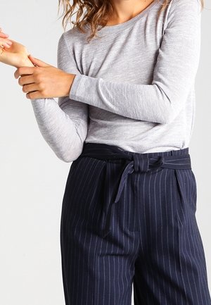Maglietta grigia chiara a maniche lunghe abbinata a pantaloni blu con righe sottili e cintura annodata. Entrambi i capi presentano una texture liscia e una vestibilità comoda.