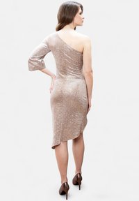 Asymetrické bodycon šaty na jedno rameno ve světle béžové barvě s lesklou texturou a jemným leopardím potiskem. Délka do poloviny stehna, rozparek na zadní straně.