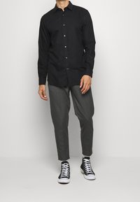 Svart långärmad skjorta med knappar, grå skräddarsydda byxor och svarta högskor. Slät tyg, figursydd design och knäppt fram.