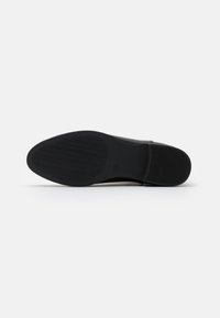 Semelle de chaussure noire à surface lisse avec un motif de semelle ondulée, conçu pour une bonne adhérence, et un léger rebord sur le périmètre.