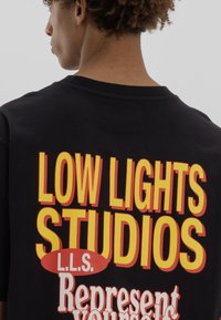 Black cotton t-shirt featuring bold yellow and red printing on the back that reads "LOW LIGHTS STUDIOS," "L.L.S.," and "Represent yourself."