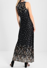 Czarna maxi sukienka w kwiatowe wzory, z dekoltem na halter i swobodną sylwetką. Posiada białe i brązowe akcenty kwiatowe na dole.