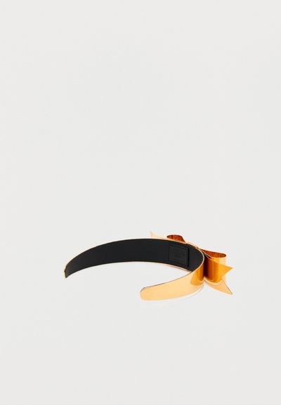 Χρυσή μεταλλική στέκα με μεγάλο φιόγκο και μαύρη επένδυση εσωτερικά, σε λευκό φόντο.