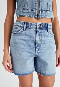 Gaiši zili džinsu šorti ar saplēstu apakšu, piecu kabatu dizains un pogu aizdare. Materiāls ir vidēja svara džins.