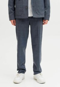 Szürke kockás öltönynadrág, testre szabott fazonnal, struktúrált anyagból készült, fehér tornacipővel párosítva a laza megjelenés érdekében.