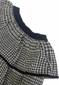 Tessuto a motivo houndstooth bianco e nero con colletto arricciato a pieghe e bordi in nero uniforme. Dettaglio della trama texturizzata.