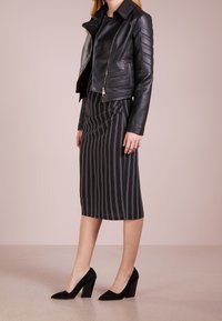 Musta nahkainen moottoripyörätakki, jossa on rakenneaksetteja, yhdistettynä tummissa sävyissä olevaan raidalliseen kynähameeseen ja mustiin mokkanahkaisiin loivakorkoisiin kenkiin.