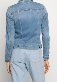 Vaaleansininen farkkutakki, jossa on sovitettu muotoilu, klassinen kaulus, napilliset hihansuut ja kaksi takana olevaa nappia säätöä varten. Näkyvät ompelusaumat.