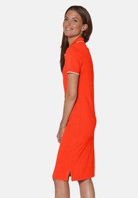 Oranges Polo-Kleid mit kurzen Ärmeln, weißen Akzenten am Kragen und an den Ärmeln, taillierte Form und einen Schlitz am Saum. Glatte Stoffoberfläche.
