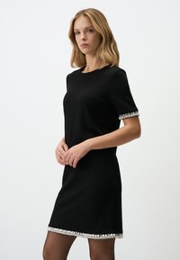 Abito nero con maniche corte, caratterizzato da un bordo decorativo di perline all'orlo e ai polsini, realizzato in un tessuto liscio con una silhouette aderente.