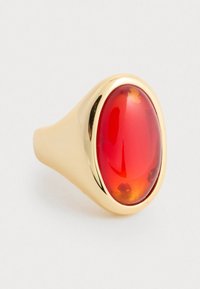 Kuldne sõrmus suure ovaalse punase kivi ja siledaga, mille pinnal on kergeid värvi variatsioone, rõhutades selle läikivat viimistlust.